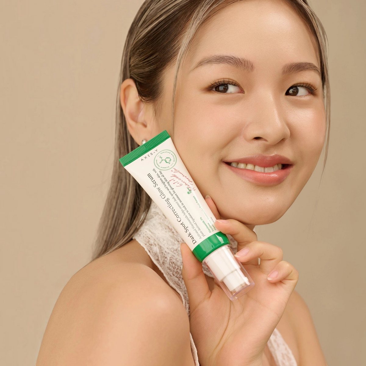 Model with glowing skin holding AXIS-Y Dark Spot Correcting Glow Serum 50ml tube beside her face