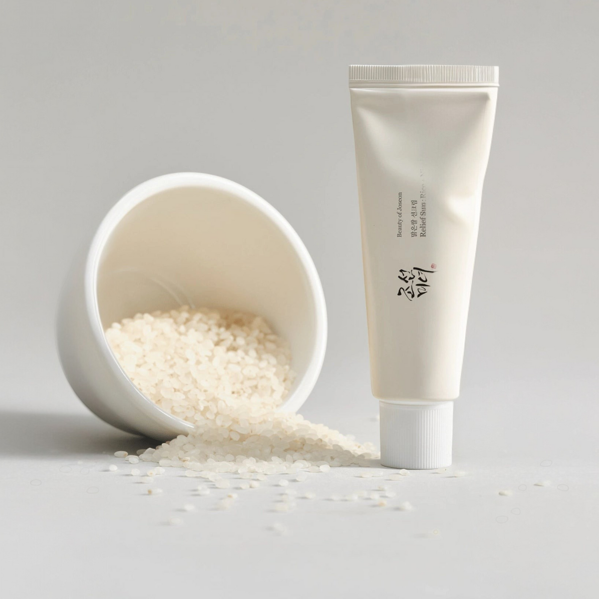 Beauty of Joseon Relief Sun: Rice + Probiotics SPF50+ PA++++ 50ml tube standing beside a tipped bowl of white rice grains